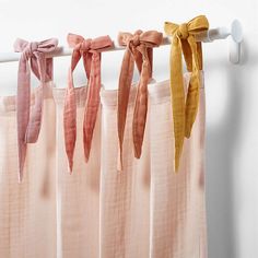 four different colored bows hanging from the side of a curtain rod in front of a white wall