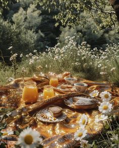 a picnic table with food and drinks on it in the middle of a field full of wildflowers