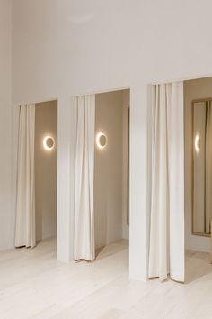 three white curtains are open in an empty room with mirrors on the wall and floor