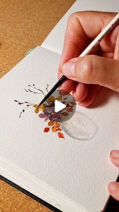 a person is drawing on paper with a pencil and watercolors in their hands