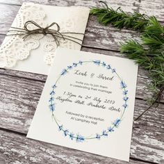 the wedding stationery is laid out on a wooden table next to some greenery