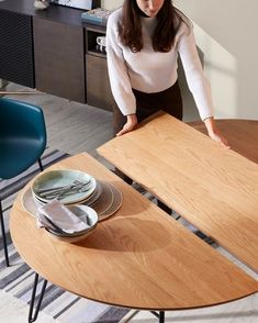 a woman standing next to a wooden table with plates and silverware in front of her