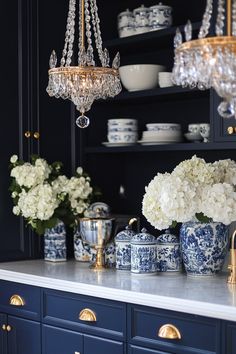 a blue and white kitchen with chandelier hanging over the island, vases filled with hydrangeas