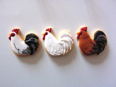 three decorated cookies in the shape of roosters on a white surface with red and black icing