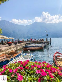 boats are docked in the water with mountains in the backgrouds and people walking around them