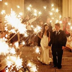 a bride and groom walk down the steps with sparklers in their hands