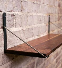 a wooden shelf mounted to the side of a brick wall next to a metal bar