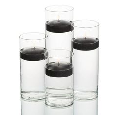 four clear glass vases with black candles in the middle one is filled with water