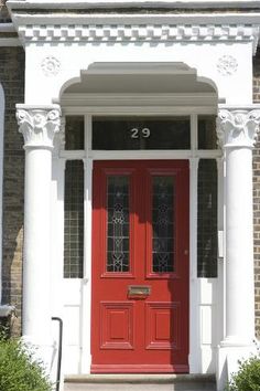 a red door is in front of a brick building with white pillars and columns on either side