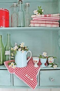 an old dresser is decorated with red and white checkered table cloths, vases, and jars