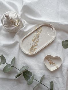 two white dishes sitting on top of a bed next to green leaves