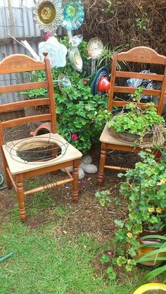 two wooden chairs sitting next to each other on top of a grass covered ground in front of a garden