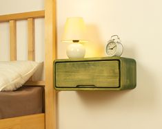 an alarm clock sitting on top of a green shelf next to a bed with a white pillow