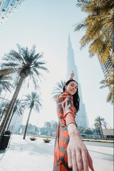 a woman in an orange and black dress is reaching out her hand to the sky