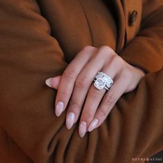 a woman's hand with a diamond ring on her left hand, wearing a brown coat