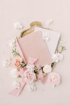 pink and white flowers surrounding an open notebook on a gold tray with ribbon around it