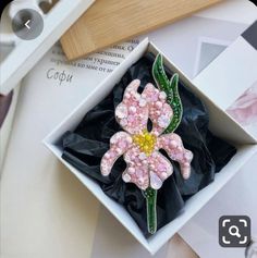 a pink flower brooch sitting inside of a white box on top of a table