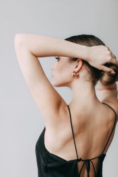 a woman in a black dress with her hands on her head and one arm behind her head