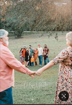 a group of people holding hands in the middle of a field with trees and grass