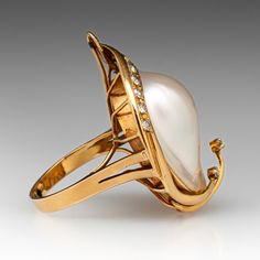 This gorgeous 18k yellow gold ring is centered with one (1) blister pearl set into a bezel. Two ribbons of yellow gold that extend over the blister pearl are accented with two (2) prong set round brilliant cut diamonds. The blister pearl is bordered with ten (10) bead set round single cut diamond accents. The ring measures 33.9mm at the top, rises 3.9mm above the finger, and tapers to 2.8mm wide by 1.0mm thick at the base of the shank.  The ring is currently a size 6.75. Luxury Yellow Gold Pearl Ring With Cabochon, Anniversary Yellow Gold Pearl Ring With Cabochon, Luxury Gold Rings With Pearl Drop, Elegant Pear-shaped Pearl Ring For Formal Occasions, Luxury High Luster Pearl Ring For Formal Occasions, Elegant Formal Pear-shaped Pearl Ring, Fine Jewelry Yellow Gold Pearl Ring With High Luster, Yellow Gold Pearl Ring With High Luster, Gold Cabochon Pearl Ring For Wedding