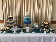 a table topped with lots of cupcakes next to a tall cake on top of a white table cloth