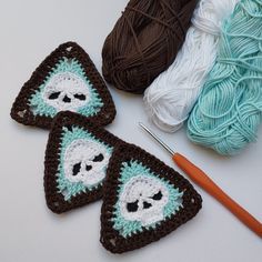 three crocheted triangulars with skulls on them next to yarn and knitting needles