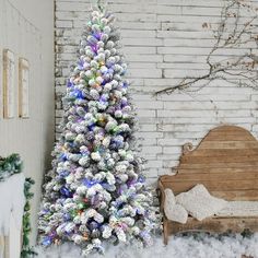 a decorated christmas tree in front of a white brick wall with snow on the ground