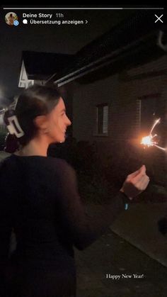 a woman holding a sparkler in her right hand while standing next to a house