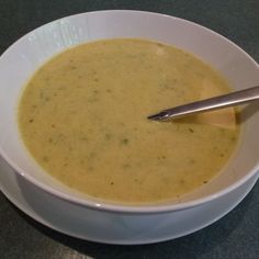 a white bowl filled with soup on top of a black counter next to a silver spoon