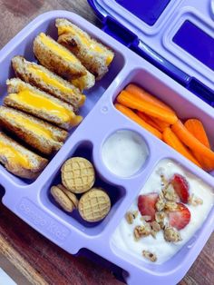 a purple lunch box filled with sandwiches, fruit and yogurt next to crackers