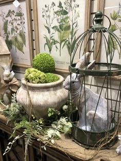 a birdcage filled with green plants next to an animal figurine