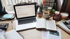 an open laptop computer sitting on top of a wooden desk next to books and magazines