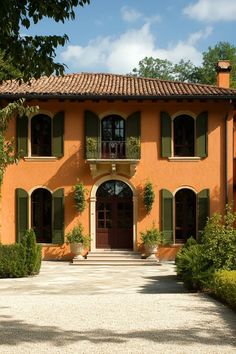 an orange house with green shutters on the front door and windows, surrounded by greenery