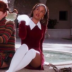 two women sitting next to each other in front of a fountain wearing matching sweaters