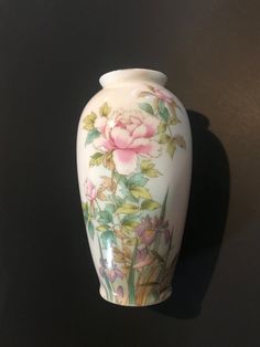 a white vase with pink flowers painted on it's sides and green leaves around the edges