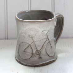 a ceramic mug with a bicycle drawn on the front and sides, sitting on a white table