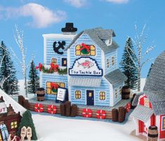 a knitted christmas scene with a blue house in the foreground and snow on the ground