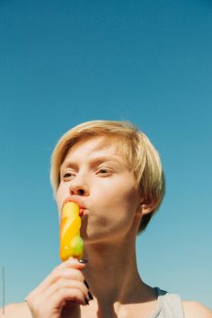 a young man is eating an orange and yellow candy bar by the beach on a sunny day