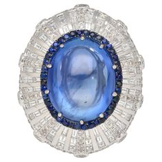 GIA Certified 26.47 Carat No Heat Sri Lanka Origin Blue Sapphire and Diamond Dome Art Deco Style Ring in 18K White Gold. Item Details: - Item Type: Cocktail Ring - Metal: 18 Karat White Gold - Weight: 14.13 Grams - Size: 6 Center Stone Details: - Type: Sapphire - Shape: Cabochon / Oval - Cutting Style: Double Cabochon - Transparency: Transparent - Color: Blue - Carat: 26.47 - Setting: Prong - Origin: Sri Lanka - Treatment: None - Measurements: 17.52 x 14.08 x 10.90 mm Side Stone Details: - 40 Ro Dome Art, Blue Star Sapphire Ring, Shades Of Dark Blue, Star Sapphire Ring, Blue Star Sapphire, Gold Cocktail Ring, Blue Sapphire Diamond, Diamond Cocktail Rings, Cabochon Ring