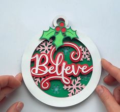 two hands holding a christmas ornament with the word believe in red and green