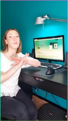 a woman sitting in front of a computer desk with a monitor and keyboard on it