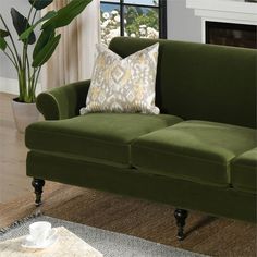 a green couch sitting in front of a window next to a table with a cup and saucer on it