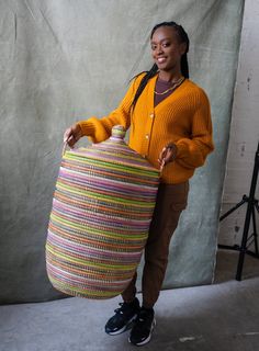 a woman standing in front of a gray backdrop holding a large round basket with braids on it