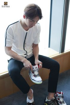 a young man sitting on top of a window sill holding a pair of sneakers