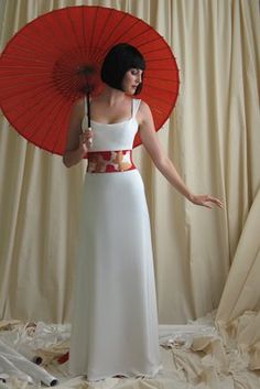 a woman in a white dress and red umbrella standing on a bed with her arms outstretched