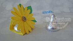 a yellow flower sitting on top of a table next to a silver candy bar wrapper