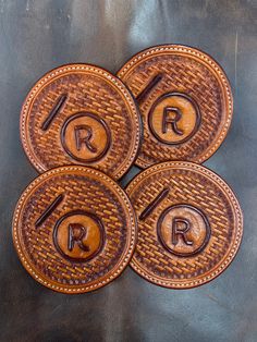 four brown leather coasters with the initials r and person on them, sitting on a black surface