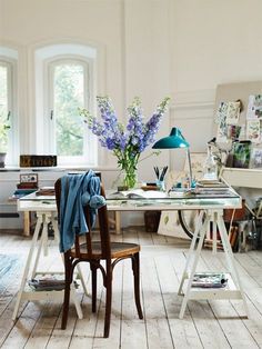 a chair and table in a room with white walls, wood flooring and large windows