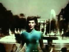 a woman standing in front of a fountain with her hands on her hips and looking at the camera