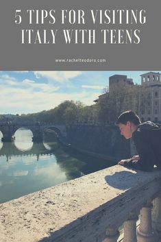 a young boy sitting on the edge of a bridge looking down at water and buildings